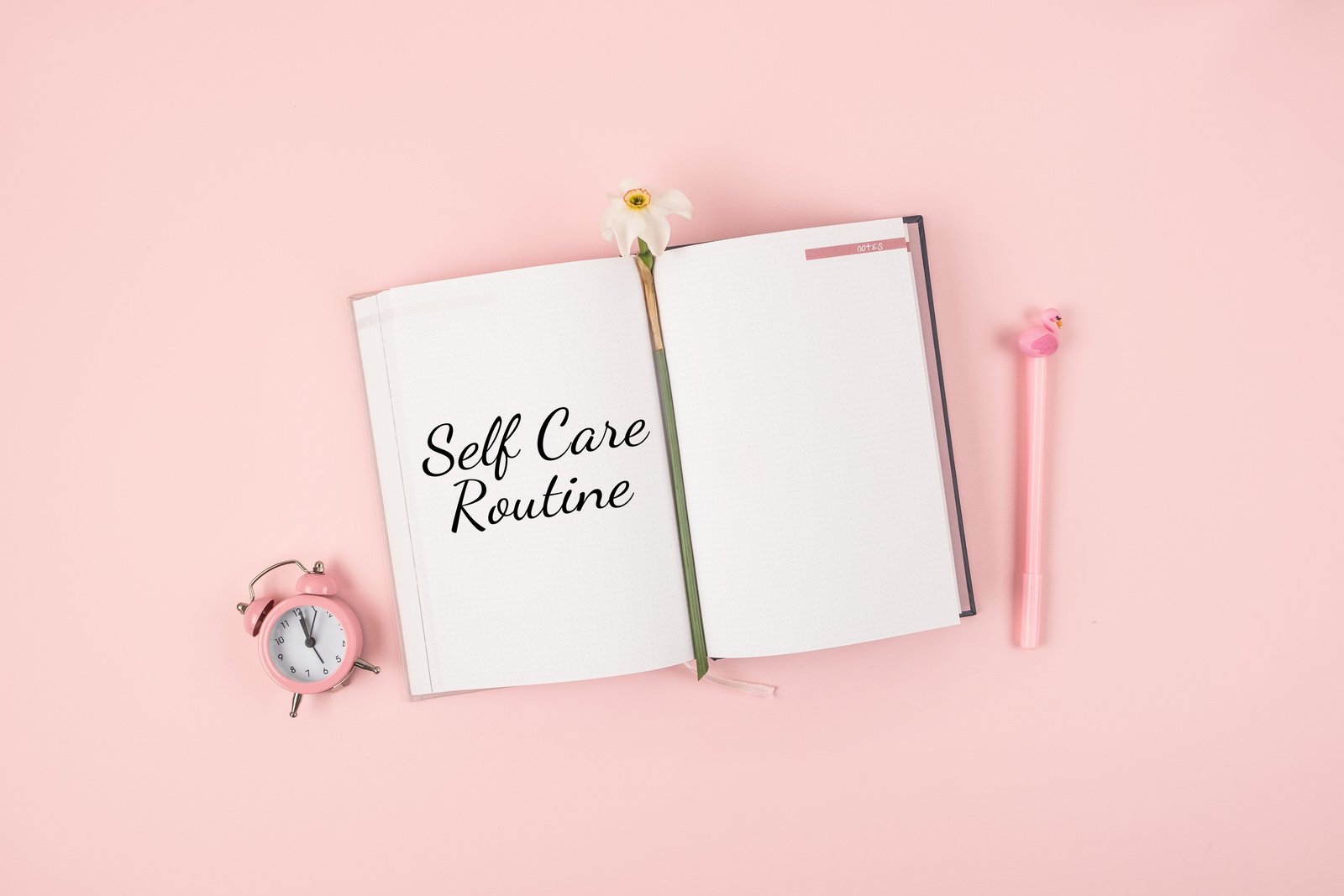 Self Care, wellbeing Routine, holistic set of self-care activities concept with open notebook, flower narcissus and alarm clock on pink background.